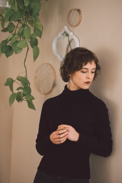 pensive young stylish lady standing near wall and looking down