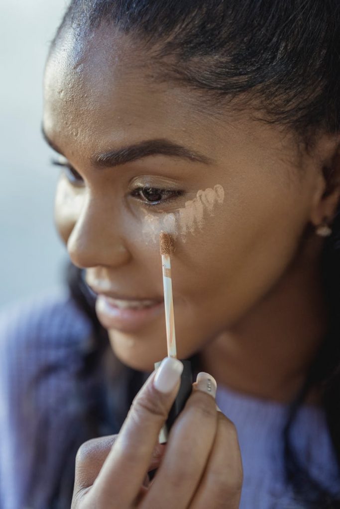 crop black woman applying concealer on face