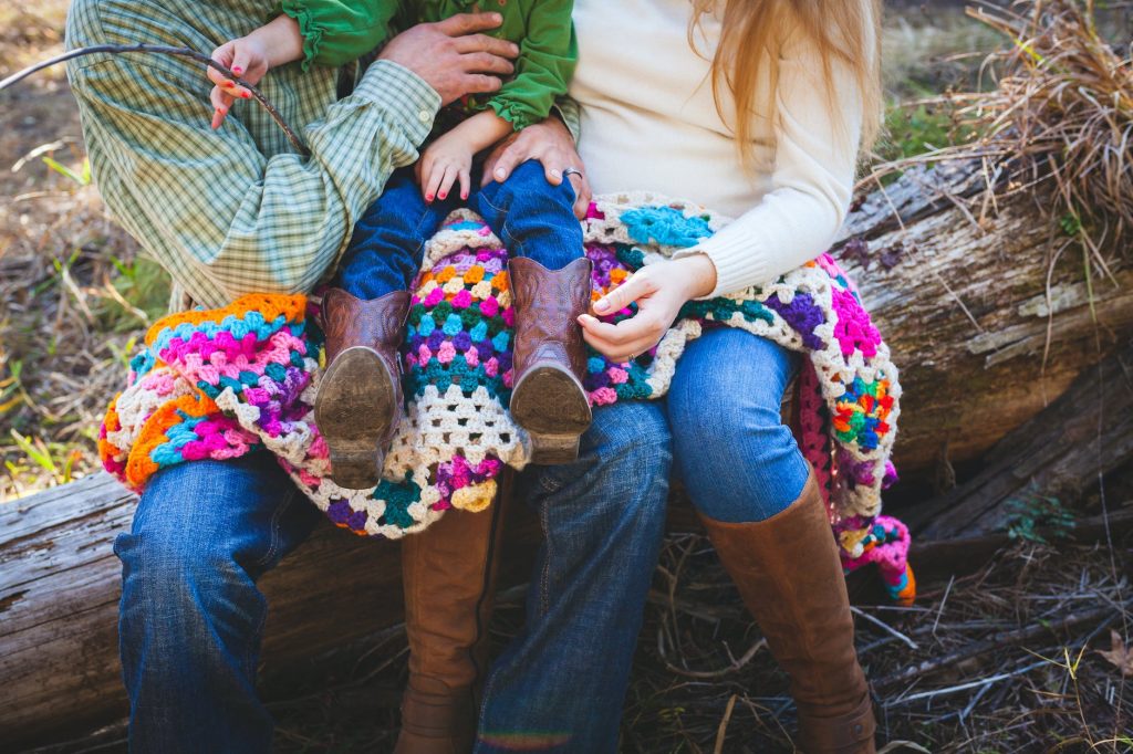 toddler sitting on person s lap while person sitting also on tree trunk